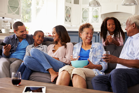 A family including parents, grandparents, a boy, and a girl sitting and smiling on the couch.