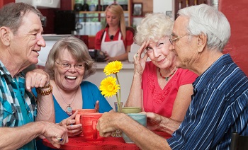 Four older people chat at a table in a cafe.