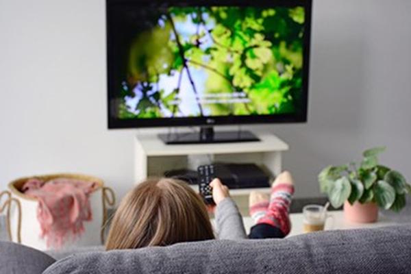 Mujer que mira televisión con subtítulos mientras está sentada en el sofá en su hogar.