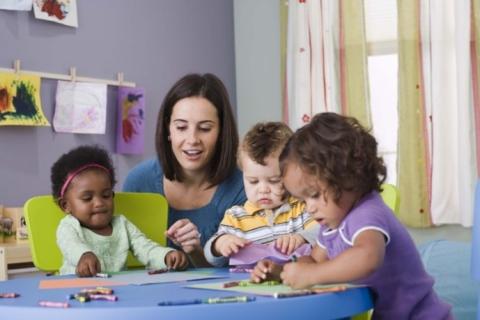 A teacher working with three toddlers who are drawing at a table.